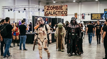 Personas disfrazadas de Stormtrooper, Yoda y Darth Vader con apariencia zombi en un pabellón con un cartel que dice Zombie Galáctico.