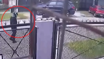 Captura de un video de seguridad donde un círculo rojo señala a una persona con casco al lado de una verja de metal y vehículos