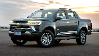 Vista frontal de tres cuartos de una Chevrolet S10 pickup gris oscuro sobre asfalto, con luces encendidas y un cielo con nubes al atardecer
