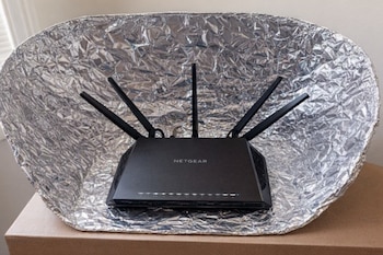 Un router WiFi Netgear negro con seis antenas sobre una mesa. Detrás hay una lámina de papel de aluminio arrugado, formando un reflector curvo.