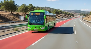 Un autobús interurbano verde con número 55 y destino Madrid circula por un carril rojo de una autovía, con árboles y montañas al fondo y cielo azul.