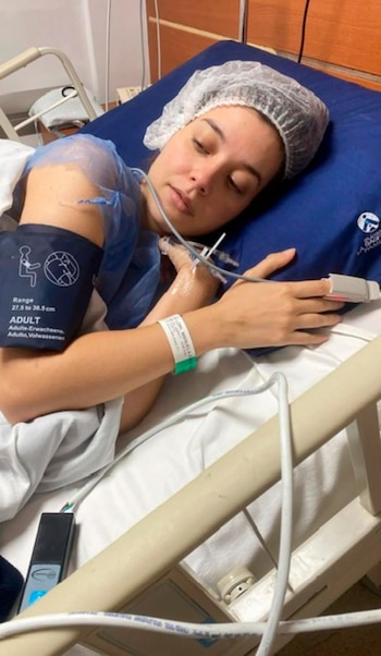 Manuela Lori en una cama de hospital, lleva un gorro quirúrgico, un brazalete de identificación y está conectada a un manguito de presión y un oxímetro