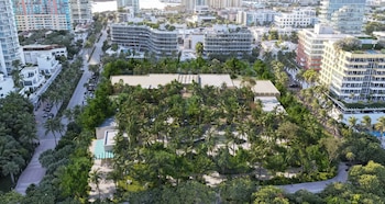 Imagen aérea de un gran complejo de edificios y vegetación, principalmente palmeras, con calles y otros edificios urbanos a su alrededor bajo un cielo claro