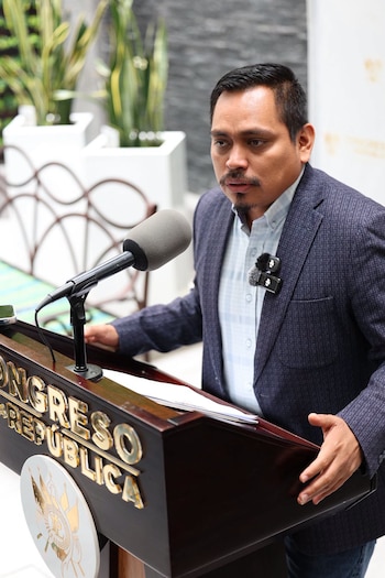 Hombre con bigote y barba corta, vestido con chaqueta, habla en un micrófono sobre un podio con texto "Congreso de la República"