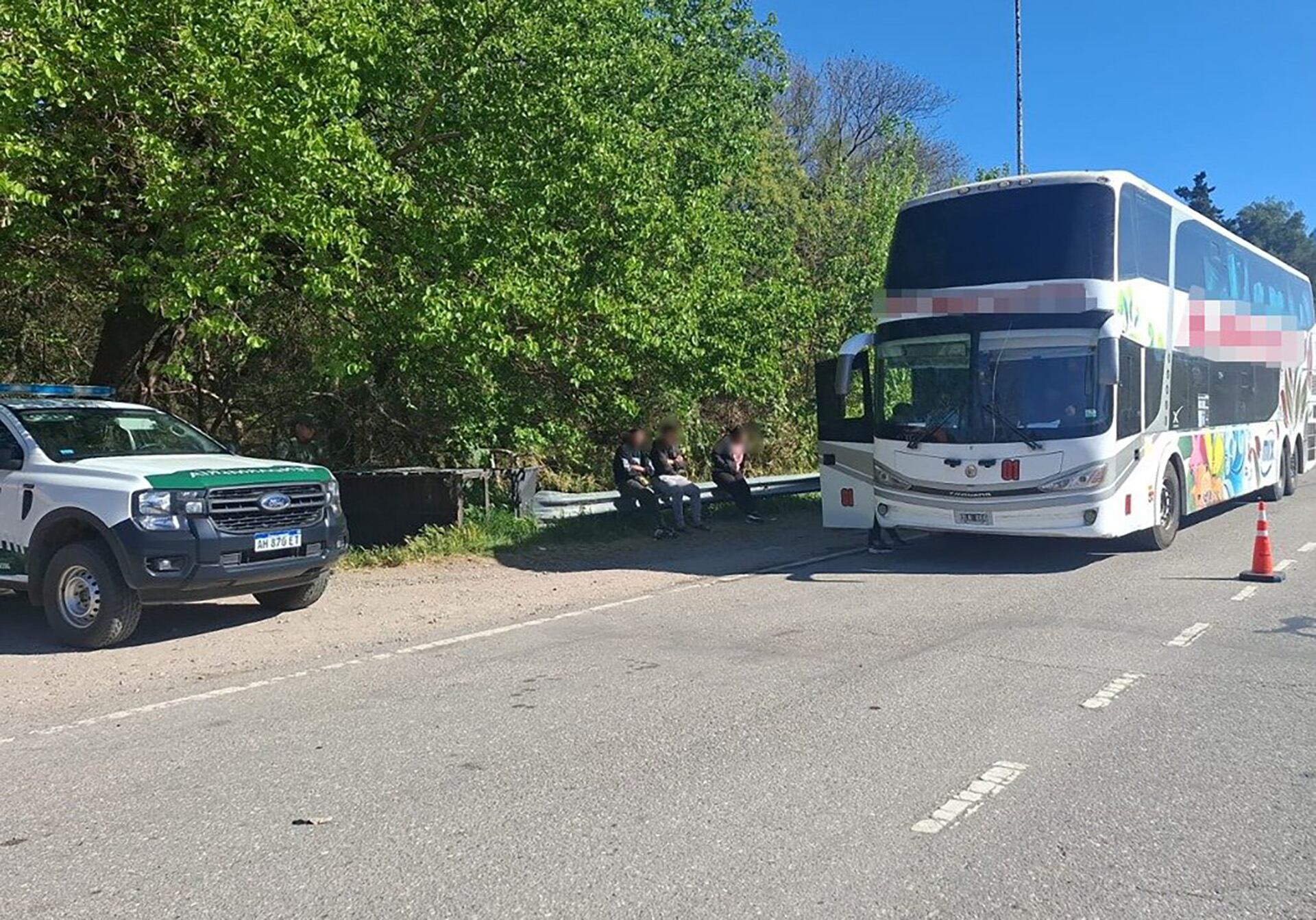 Un autobús de turismo permanece detenido en el arcén de una carretera junto a un vehículo de seguridad y un grupo de pasajeros.