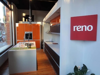Vista interior de un showroom de cocinas. Una isla blanca con fregadero y grifo, gabinetes naranjas y un cartel rojo con "reno" en la pared