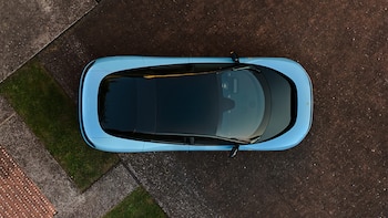 Vista aérea de un Ferrari Luce azul claro con techo negro, aparcado en un camino pavimentado con secciones de césped al borde