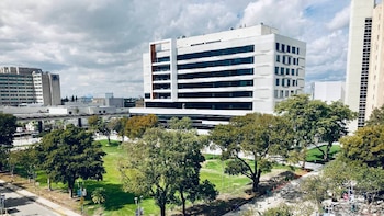 Vista aérea de un área urbana con edificios de gran altura modernos, un parque verde con árboles frondosos y un cielo nublado