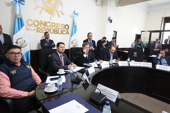 Hombres en una reunión formal sentados alrededor de una mesa de conferencia. Al fondo se ve la inscripción "CONGRESO DE LA REPÚBLICA" y banderas nacionales