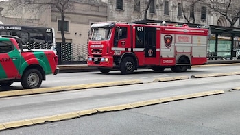 Un camión rojo de bomberos y una camioneta médica permanecen detenidos en la calzada junto a una parada de autobús