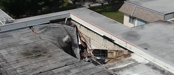 Vista aérea de un techo plano de edificio con una gran sección colapsada, que muestra escombros, estructura dañada y paredes interiores expuestas