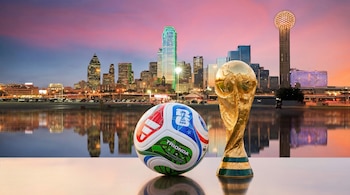 Pelota oficial del Mundial FIFA 2026 y Copa del Mundo dorada en primer plano con el skyline de Dallas, incluyendo Reunion Tower, al atardecer, reflejado en agua.
