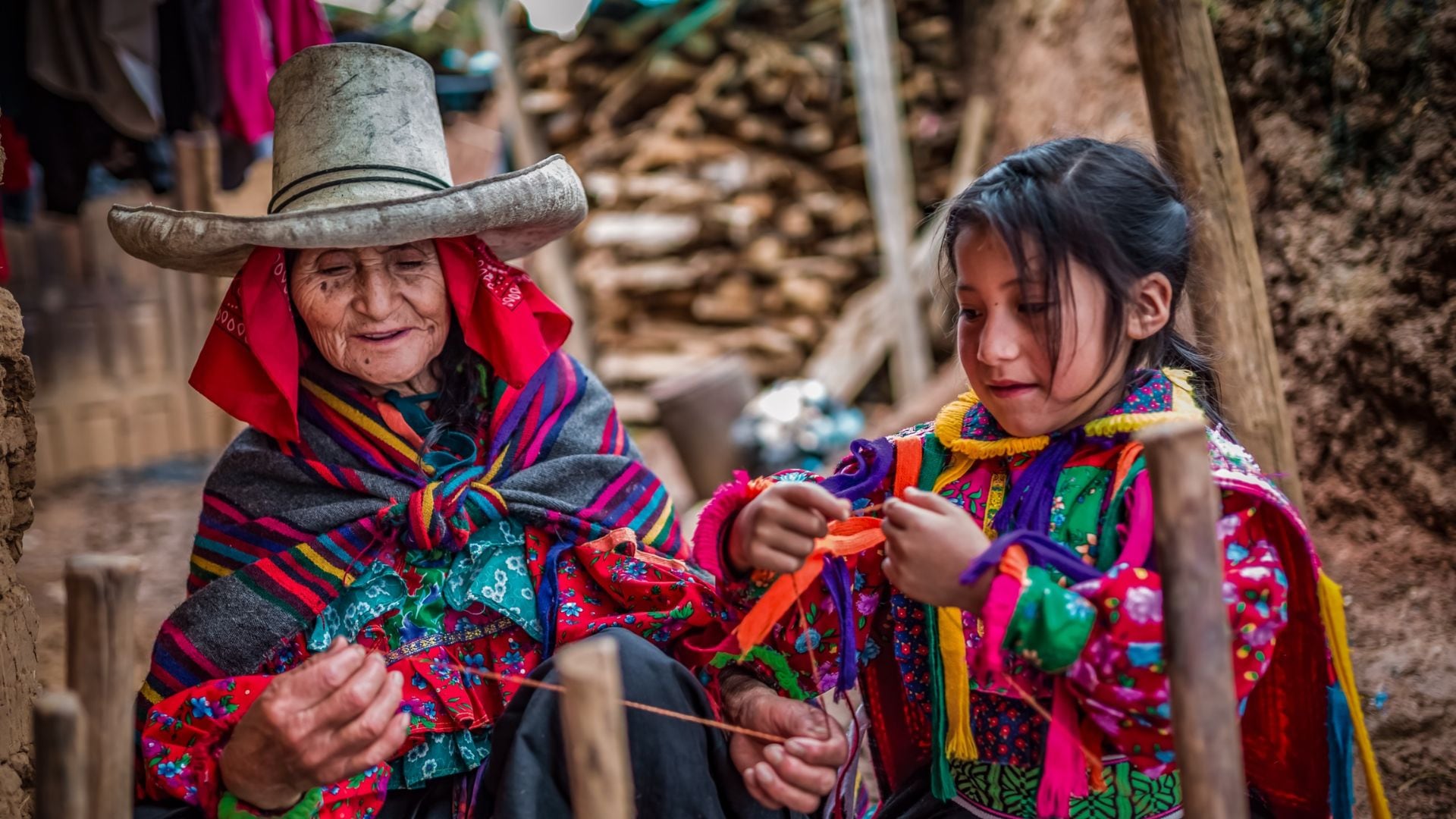 Una anciana y una niña, vestidas con trajes tradicionales coloridos, comparten un momento de enseñanza y aprendizaje en el arte del tejido ancestral. (MIDIS)