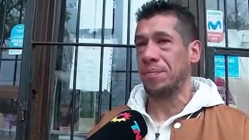 Un hombre con chaqueta marrón y capucha blanca habla frente a un micrófono de prensa ante una puerta con rejas