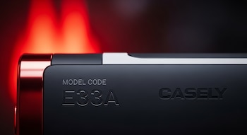 Primer plano del reverso de una batería externa Casely Power Pod negra. Se ven los caracteres 'MODEL CODE E33A' y el logo 'CASELY' grabados. Fondo oscuro con un brillo rojo.