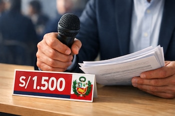 Primer plano de una mano masculina sosteniendo un micrófono y papeles, con un cartel de S/1.500 y el escudo de Perú sobre una mesa de madera clara.