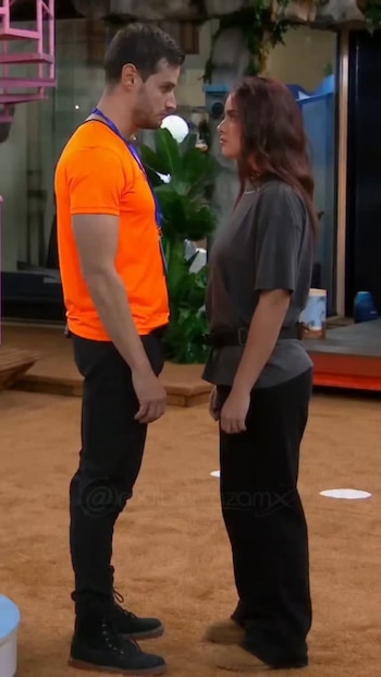 Un hombre con camiseta naranja y una mujer con camiseta oscura están de pie mirándose de frente en un espacio interior