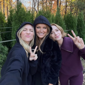 Tres mujeres, Malin Akerman, Brittany Snow y Jaime Ray Newman, posan sonriendo y haciendo el signo de la paz al aire libre con vegetación de fondo