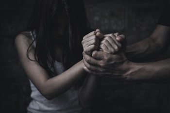 Primer plano de las manos de un hombre agarrando firmemente las manos entrelazadas de una joven. La joven tiene el cabello oscuro y mira hacia abajo.
