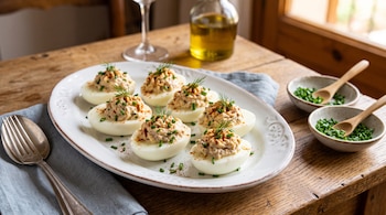 Seis mitades de huevos rellenos con crema, especias y cebollino dispuestas en una fuente blanca sobre una mesa de madera.