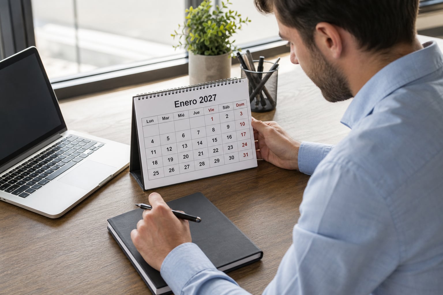 Un trabajador revisa un calendario de enero de 2027 mientras toma notas en su mesa de oficina. (Imagen Ilustrativa Infobae)