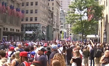 Vista de una gran multitud en una calle urbana, con muchas banderas puertorriqueñas. Edificios y un letrero de PUMA son visibles
