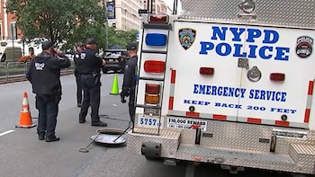 Parte trasera de un camión del servicio de emergencia de la Policía de Nueva York y cuatro agentes junto a una alcantarilla abierta