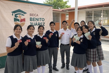 Grupo de jóvenes estudiantes mexicanos, uniformados, sonriendo y mostrando tarjetas bancarias o billetes frente a una lona del programa Beca Benito Juárez.