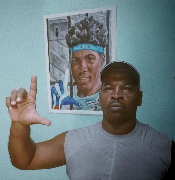 El activista Félix Navarro Rodríguez realiza la señal de libertad con la mano frente a un retrato colgado en una pared. (Cortesía: Observatorio Cubano de Derechos Humanos)