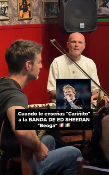 Dos hombres tocan instrumentos musicales en una habitación con paredes rojas, cuadros y un altavoz, con una imagen incrustada de Ed Sheeran y texto