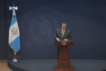 Bernardo Arévalo habla frente a un micrófono en un podio de madera junto a la bandera de Guatemala sobre un fondo azul