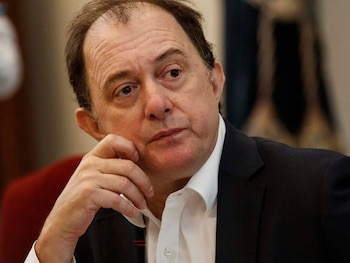 Primer plano de Iván Poduje, un hombre de mediana edad con cabello castaño oscuro, traje oscuro y camisa blanca, con la mano derecha apoyada en la barbilla y mirando hacia la derecha