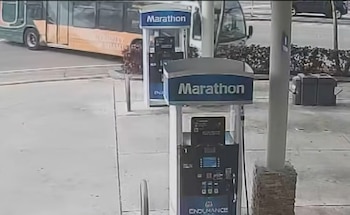 Vista aérea de un autobús verde y naranja de la Universidad de Miami pasando por una estación de servicio Marathon con dos surtidores visibles