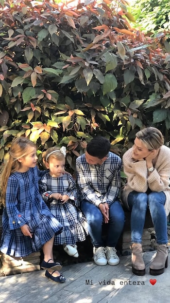 Evangelina Anderson y sus tres hijos sentados en un banco de piedra frente a un arbusto frondoso de hojas verdes y rojizas