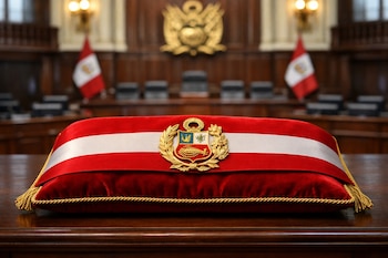 Banda presidencial peruana roja y blanca con escudo dorado sobre cojín de terciopelo rojo. Detrás, banderas de Perú, escudo nacional y asientos vacíos del Congreso.