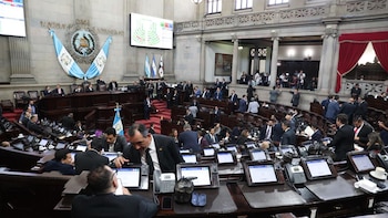 Vista general del hemiciclo del Congreso de Guatemala con numerosos diputados sentados y de pie; banderas de Guatemala y pantallas electrónicas visibles