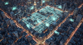 Vista aérea de una ciudad con rascacielos y calles iluminadas por el tráfico, superpuesta con una cuadrícula digital azul brillante y puntos que indican datos de emisiones.