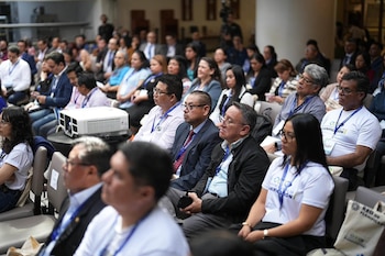 Un grupo de personas sentadas en filas dentro de un salón de actos observa una presentación junto a un proyector