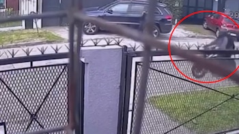 Captura de cámara de seguridad con una reja en primer plano, vehículos al fondo y una persona en motocicleta rodeada por un círculo rojo