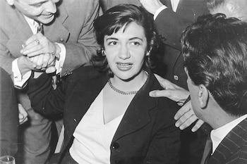 Fotografía en blanco y negro de una mujer sentada mientras personas con traje la rodean y le estrechan la mano