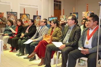 Personas sentadas en hilera con hojas de papel en las manos frente a varias pinturas religiosas dispuestas sobre caballetes