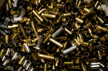 Primer plano de una gran pila de casquillos de bala vacíos, predominando los de color dorado de latón, mezclados con algunos de aleación plateada