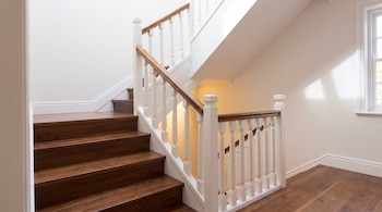 Escalera de peldaños de madera oscura con barandilla de barrotes blancos y pasamanos de madera junto a paredes claras y una ventana.