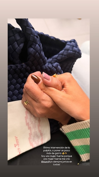 Dos manos entrelazadas en primer plano, una con uñas marrones y la otra con diseño francés rosa y blanco. Fondo oscuro y parte de una prenda a rayas verde y beige