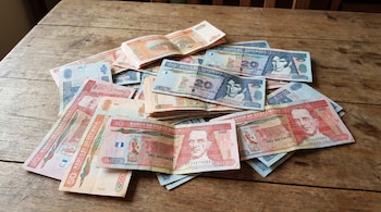 Fotografía de varios billetes de quetzal guatemalteco de 10, 20 y 50, desordenados sobre una mesa de madera con vetas visibles y textura.