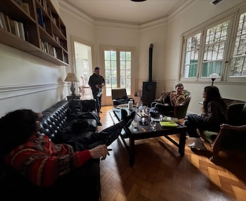 Cuatro personas conversan en la sala de una casa con mesa de centro, biblioteca de madera y piso de parqué