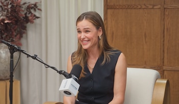 Jennifer Garner, vestida con un chaleco oscuro, sonríe sentada junto a un micrófono de estudio