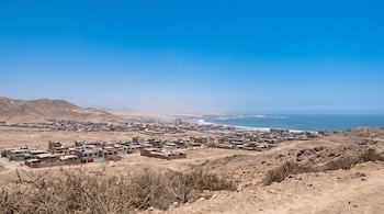 Vista panorámica de edificaciones en un terreno desértico junto a cerros áridos y el océano Pacífico bajo un cielo azul despejado.