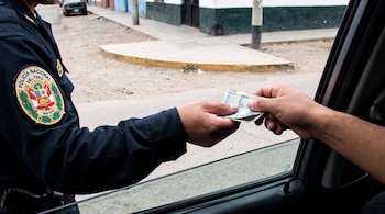 Mano de policía uniformado de Perú recibiendo billetes de otra mano que sale de la ventanilla de un vehículo. Fondo de calle.