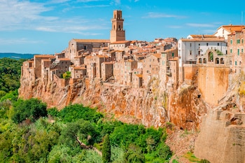 Edificaciones de piedra con tejados rojos y una torre campanario se ubican al borde de un precipicio rocoso rodeado de vegetación